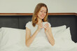 © rohappy - Happy smiling young woman enjoying with cup of hot coffee lying on bed at home