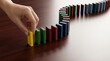 © CK Studio - Hand placing colorful dominoes on a wooden table, symbolizing cause and effect, strategy, planning, and the start of a new process.