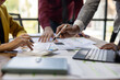 © Wasan - Business people analyzing financial charts and documents using calculator and laptop during a working meeting discussing company strategy and planning.