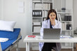 © Wasan - Female doctor smiling and working on laptop in medical office.