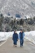 © Creativa Images - ​A couple walks hand-in-hand down a snow-covered mountain road, flanked by deep snowdrifts and a dense, snowy forest backdrop in winter