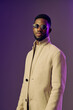 © SHOTPRIME STUDIO - Stylish young Black man in a beige coat and sunglasses posing against a purple backdrop, exuding confidence and fashion forward vibes