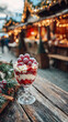 © Nad - A glass filled with layers of cream and raspberries sits on a wooden table. Colorful lights glow from stalls in the background, giving a warm evening feeling.