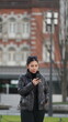 © Creativa Images - A young woman wearing a black puffer jacket and sunglasses on her head stands outdoors looking at her smartphone, with a blurred, historic Tokyo Station in the background
