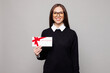 © ViDi Studio - Young successful employee business woman corporate lawyer wear black sweater glasses shirt work in office hold gift certificate coupon voucher card for store isolated on plain grey color background.