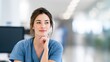 © Дмитрий Баронин - Woman in blue scrubs thoughtfully considering ideas while sitting in a bright, modern healthcare environment, showcasing contemplation and professionalism in a medical setting