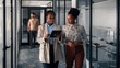 © Jelena - Two Professional Women Collaborating in Office Hallway Environment