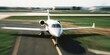 © ekaterina - A white private jet on a runway at an airport. The aircraft is positioned for takeoff with a blurred background of grass and airport buildings.