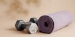 © progressman - Pair of dumbbells and a yoga mat are on a tan surface