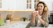 © New Africa - Smiling woman in headphones with cup listening music at table in kitchen