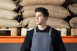 © Artem Varnitsin - Portrait of a young male wearing an apron standing in a warehouse against bags of coffee beans