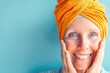 © Evhen Pylypchuk - Brightly lit portrait of a joyful Eastern woman with an orange headband, gently touching her cheeks, smiling warmly at the camera against a blue background