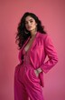 © Maryna - Woman in pink pantsuit poses confidently. She wears large hoop earrings and a bracelet. Her curly dark hair flows around her shoulders. Modern bold aesthetic style in studio.