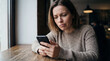 © MYKHAILO KUSHEI - A woman sits in a cafe, gazing intently at her phone screen. Her brow furrows, suggesting she is confused or concerned by what she sees on her mobile device.