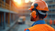 © Vadym - Construction worker in orange hard hat and earmuffs looks over building site. Man wears blue shirt and hi vis vest. Safety gear protects hearing and head.