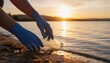 © Igor_Tichonow - Gloved hands picking up a discarded plastic bottle from the shoreline at sunset symbolizing environmental responsibility conservation awareness and community cleanup efforts