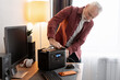 © Maria Vitkovska - Senior man plugging smart device into portable power station at home office desk