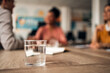 © Jelena - Close-Up Glass of Water With People Discussing in the Background