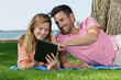 © auremar - couple layed on grass in the park looking at tablet