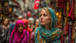 © dominic - Young woman wearing patterned blue headscarf and red jacket walking through crowded outdoor market street with colorful fabrics and flags hanging above in daytime