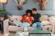 © Jose Calsina - Happy couple sharing a moment while using a smartphone to explore an app on their cozy couch together, enjoying their time in a warm and inviting home atmosphere filled with love and connection.