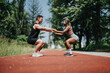 © qunica.com - A man and woman engaging in partnered squats on a running track surrounded by greenery.