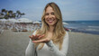 © Krakenimages.com - Blonde woman hands showing money sign gesture at beach; wealth prosperity playfulness spending vacation.
