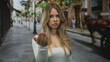 © Krakenimages.com - Blonde woman with focused expression beckoning with hand in white top on busy urban street; invitation impatience.