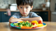 © photo for everything - A little boy with a face of displeasure, sitting at the table. Vegetables are in front of him on a colorful plate. The child seems reluctant to eat the healthy meal.