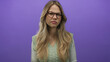 © Krakenimages.com - Blonde woman wearing glasses and green sweater vest furrows brow in purple studio set; frustration doubt.