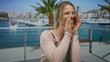 © Krakenimages.com - Woman in apron with blonde hair tied back laughs while cupping hands at mouth at sunlit port; joy playfulness.