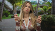© Krakenimages.com - Woman making air quotes gesture with fingers and raised eyebrows in a tropical green park; sarcasm doubt.
