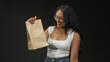 © Krakenimages.com - Woman holds paper bag high while pumping fist in studio, wearing white tanktop and jeans with glasses, smiling broadly; celebration success reward.