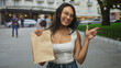 © Krakenimages.com - Woman holding paper bag pointing finger on a city street, smiling and offering the package; casual playful promotion.