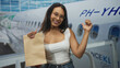 © Krakenimages.com - Woman holds paper bag with left hand and raises thumb up gesture at airport gate while smiling; travel excitement.