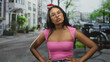 © Krakenimages.com - Young hispanic woman with hands on hips wearing pink top and glasses, bare shoulders visible, looking up on a street lined with buildings and bicycles; confidence assertiveness poise.