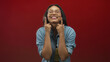 © Krakenimages.com - Woman cupping face with hands while smiling and tilting head, wearing glasses and denim shirt in red studio; playful joy.