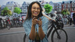 © Krakenimages.com - Woman pointing fingers at camera on a busy street lined with parked bicycles and city buildings; playful spontaneity.