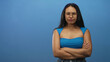 © Krakenimages.com - Woman arms crossed, pursed lips and glasses against blue studio backdrop wearing sleeveless top and jeans; skepticism contemplation.