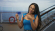 © Krakenimages.com - Brunette woman with glasses holds blue creditcard and points finger at card on ship deck near lifebuoy and railing; travel convenience confidence.