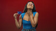 © Krakenimages.com - Woman holding creditcard with hand on neck and grimacing in studio red setting; financial stress discomfort.