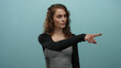 © Krakenimages.com - Young woman pointing against isolated blue background with serious expression suggesting determination.