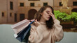 © Krakenimages.com - Woman standing outdoors holding shopping bags on a city street with an expression of exhaustion after shopping