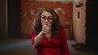 © Krakenimages.com - Woman wearing red shirt and glasses gesturing at construction site with expression of focus amid brick walls in progress indoors conveying assertive interaction
