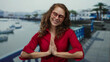 © Krakenimages.com - Woman smiling in red shirt by seaside promenade with blurred boats and buildings in background, embodying joy and relaxation on a sunny beach day.