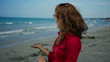 © Krakenimages.com - Woman in red shirt extends her hands at a seaside beach with turquoise water and sands, showcasing a joyful expression while embracing the natural outdoor environment.