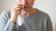 © evastock - Middle-aged woman with a slightly reddened nose pressing a tissue against the nose, upper body leaning a bit, image framed from just below the eyes downward, neutral uncluttered background.