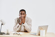 © SHOTPRIME STUDIO - Portrait of surprised young man with dark skin, sitting at desk in bright modern office with laptop, eyeglasses, and stationery on table. Male expression of shock or disbelief. Studio shot with