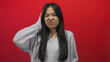 © Krakenimages.com - Young chinese woman with long hair in a sweater looks puzzled and thoughtful against a vibrant red background wall.