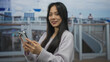 © Krakenimages.com - Young chinese woman enjoying a scenic cruise on a boat by the seaside outdoors, smiling and using a smartphone with modern technology surrounding her on a sunny day.